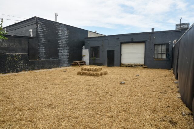 Outdoor area with hay and dark building.